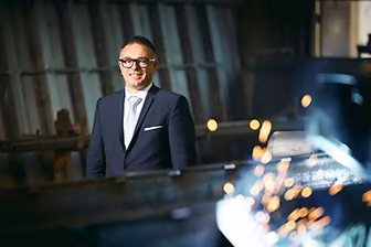 Homme en complet souriant debout dans un atelier de fabrication avec des étincelles en avant-plan
