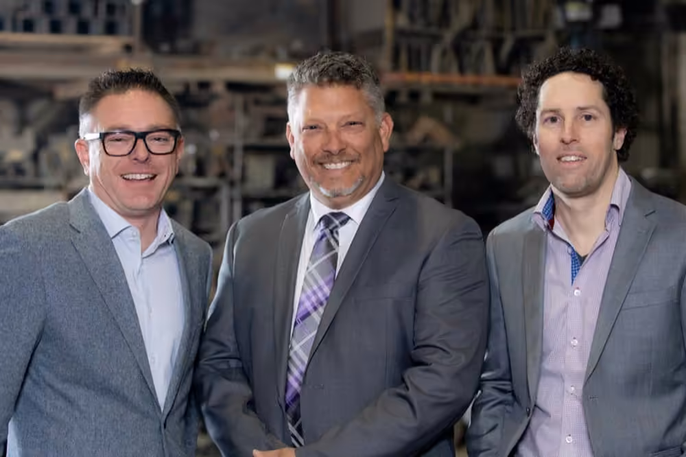Trois hommes en veston souriant dans un environnement industriel