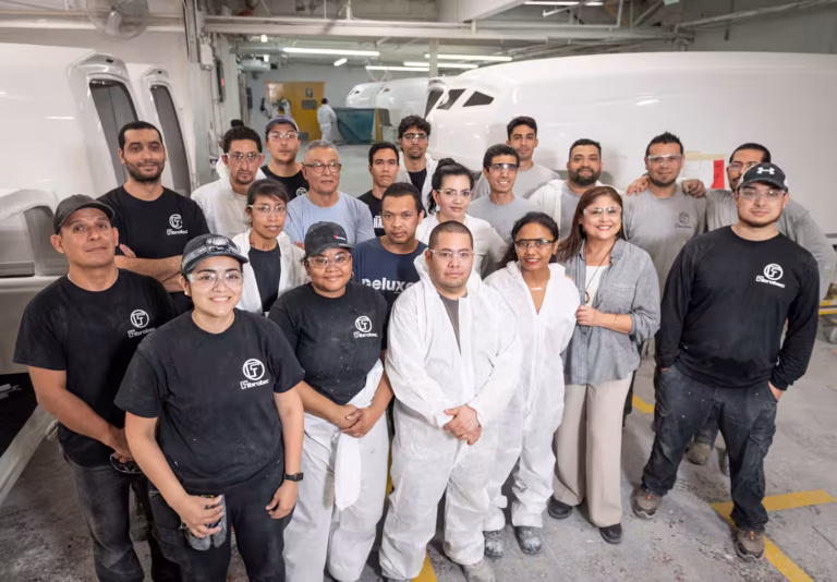 Groupe d'ouvriers et techniciens en atelier de fabrication devant des pièces d'avion blanches