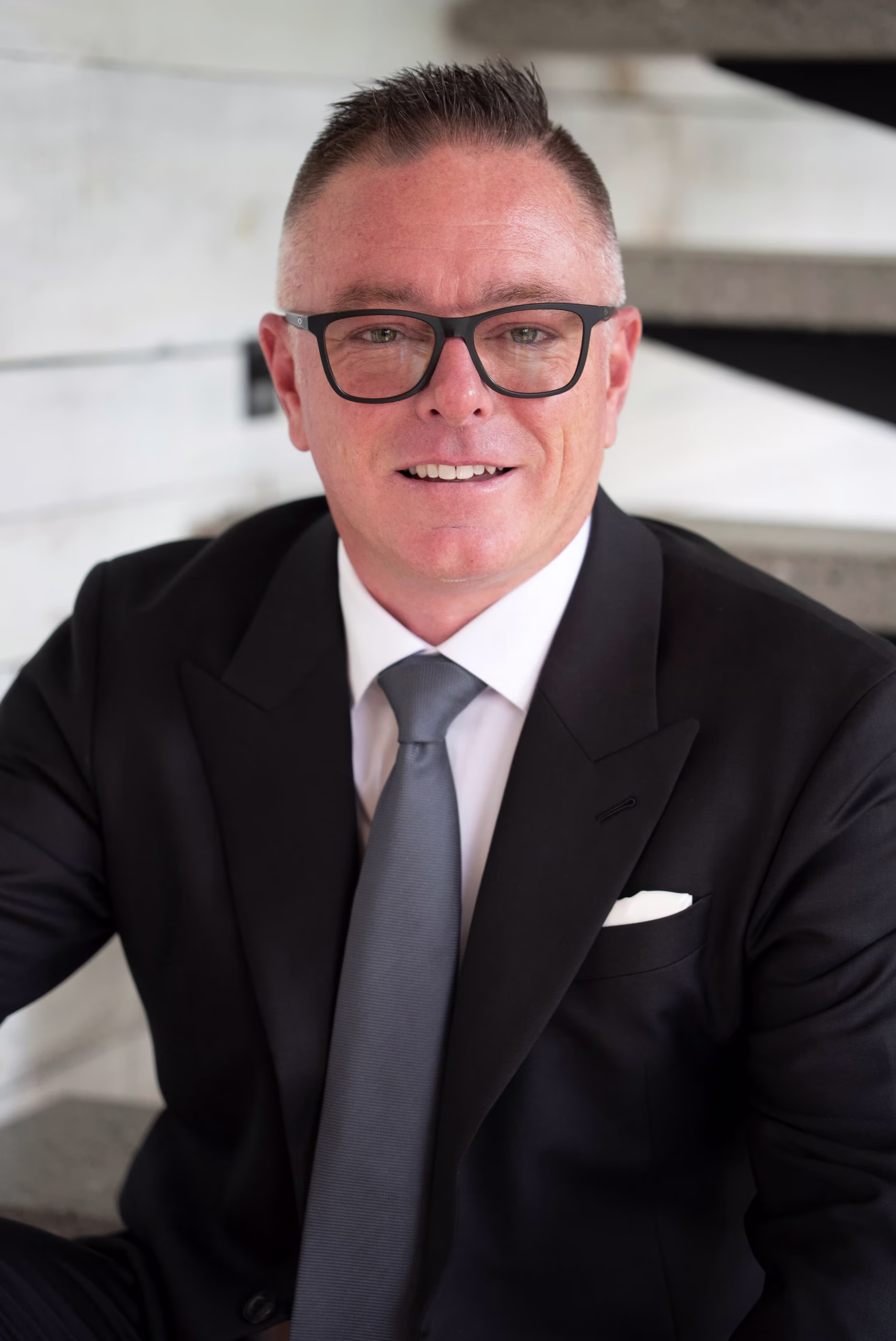 Homme d'affaires souriant portant des lunettes, un complet noir et une cravate gris